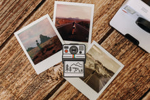 Load image into Gallery viewer, Wildtree Outdoor Photographer Polaroid sticker sitting on wood floor surrounded by polaroid photos
