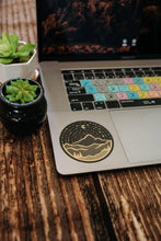 Load image into Gallery viewer, Laptop on wood background with wildtree mountain adventure sticker placed on laptop
