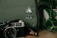 Load image into Gallery viewer, Recycle logo redesigned incorporating a mountain and tree pinned to a backpack above a camera pin and camera.
