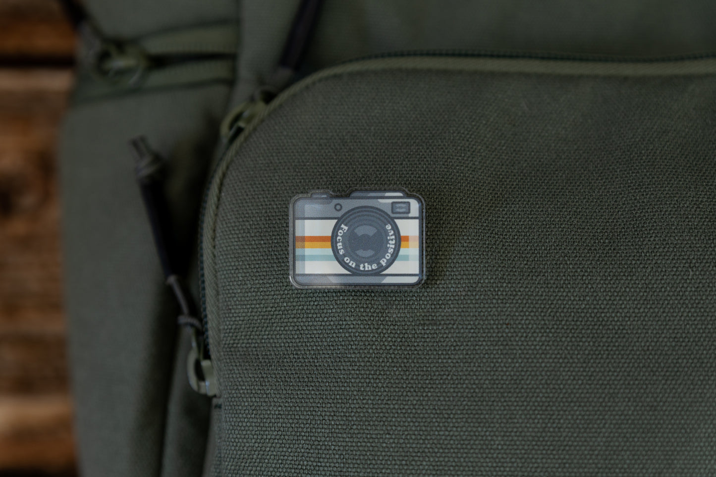 Focus on the positive Retro Camera Acrylic Pin on green backpack