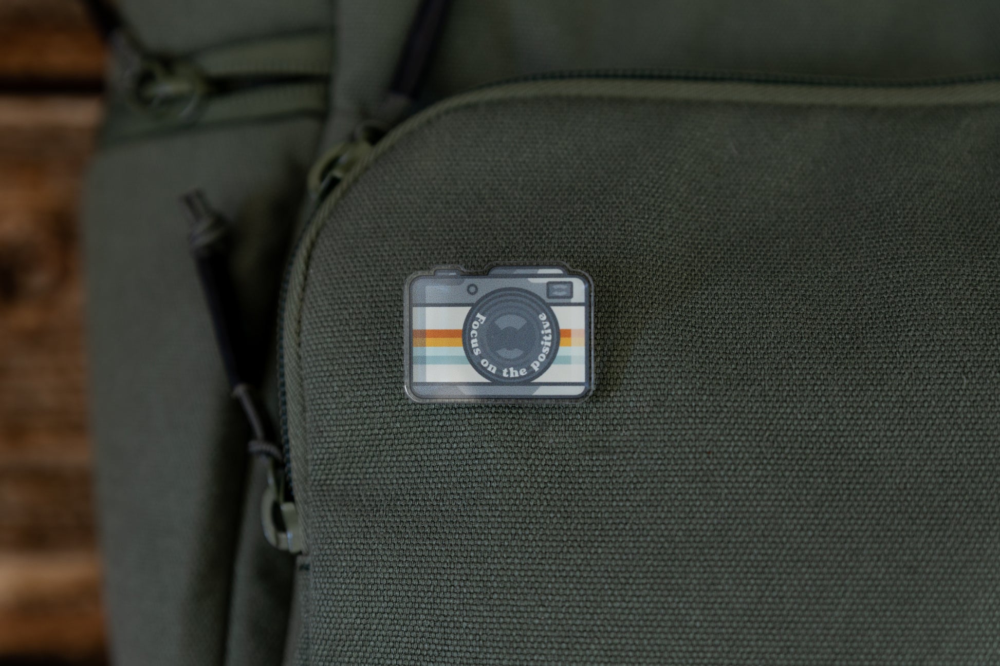 Focus on the positive Retro Camera Acrylic Pin on green backpack