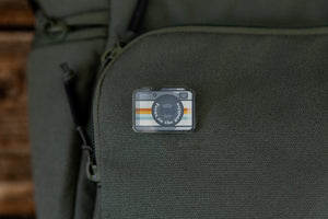 Focus on the positive Retro Camera Acrylic Pin on green backpack