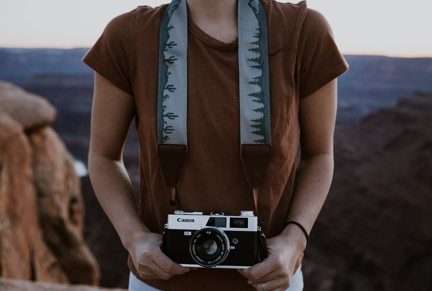 Women holding camera with Wildtree cactus and pine tree camera strap around neck