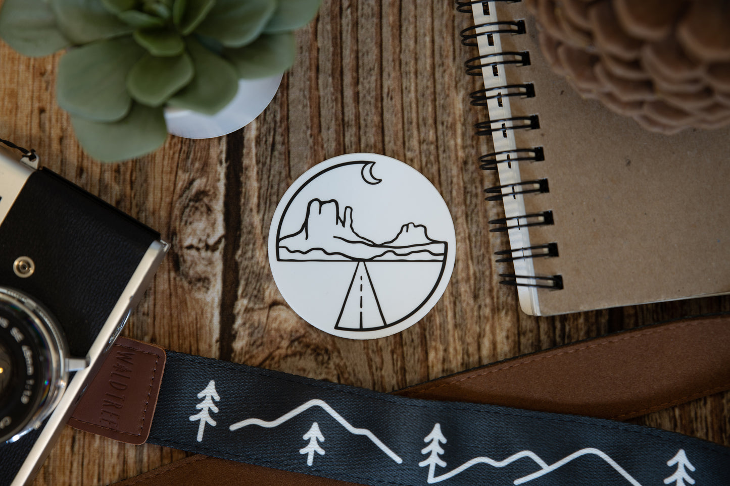 Circle Monument valley sticker on wood background surrounded by notebook, camera and succulent