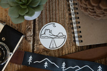 Load image into Gallery viewer, Circle Monument valley sticker on wood background surrounded by notebook, camera and succulent

