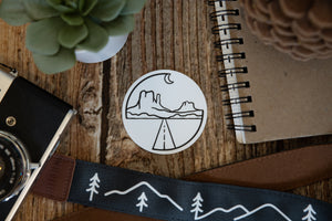Circle Monument valley sticker on wood background surrounded by notebook, camera and succulent