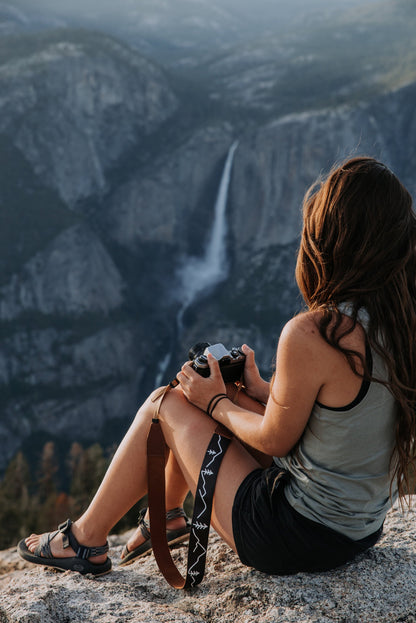 Women sitting overlooking waterfall holding film camera and Wildtree camera strap