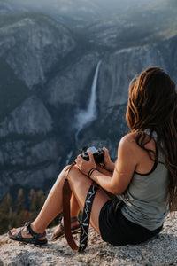 Women sitting overlooking waterfall holding film camera and Wildtree camera strap