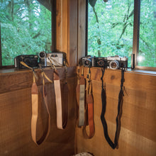 Load image into Gallery viewer, collection of wildtree solid colored camera straps sitting on window

