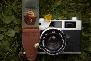 Smokey Bear camera strap next to flowers and film camera