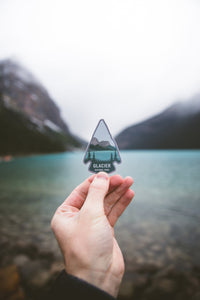 hand holding glacier national park sticker in front of a lake in glacier national park