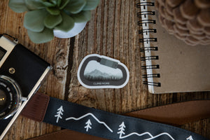 Climb More Carabiner Sticker on wood background surrounded by notebook, camera and succulent 