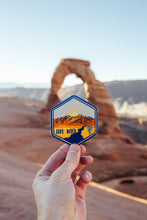 Load image into Gallery viewer, hand holding wildtree live wild iron on patch in front of delicate arch utah
