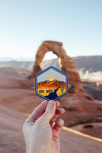 hand holding wildtree live wild iron on patch in front of delicate arch utah