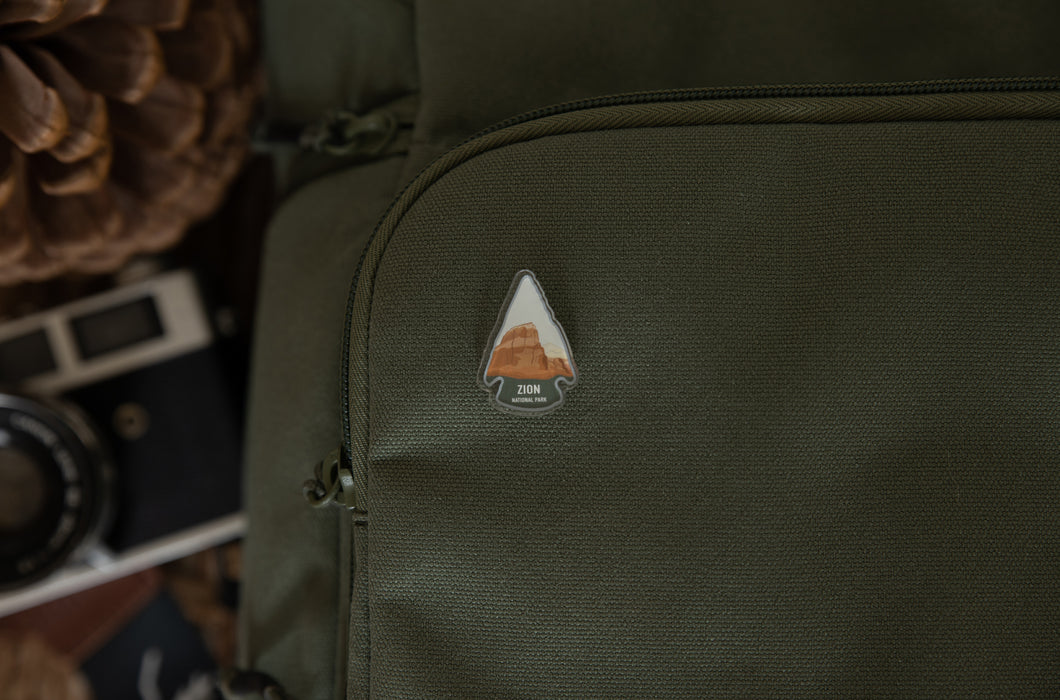 Zion National Park pin in shape of arrow head pinned on backpack